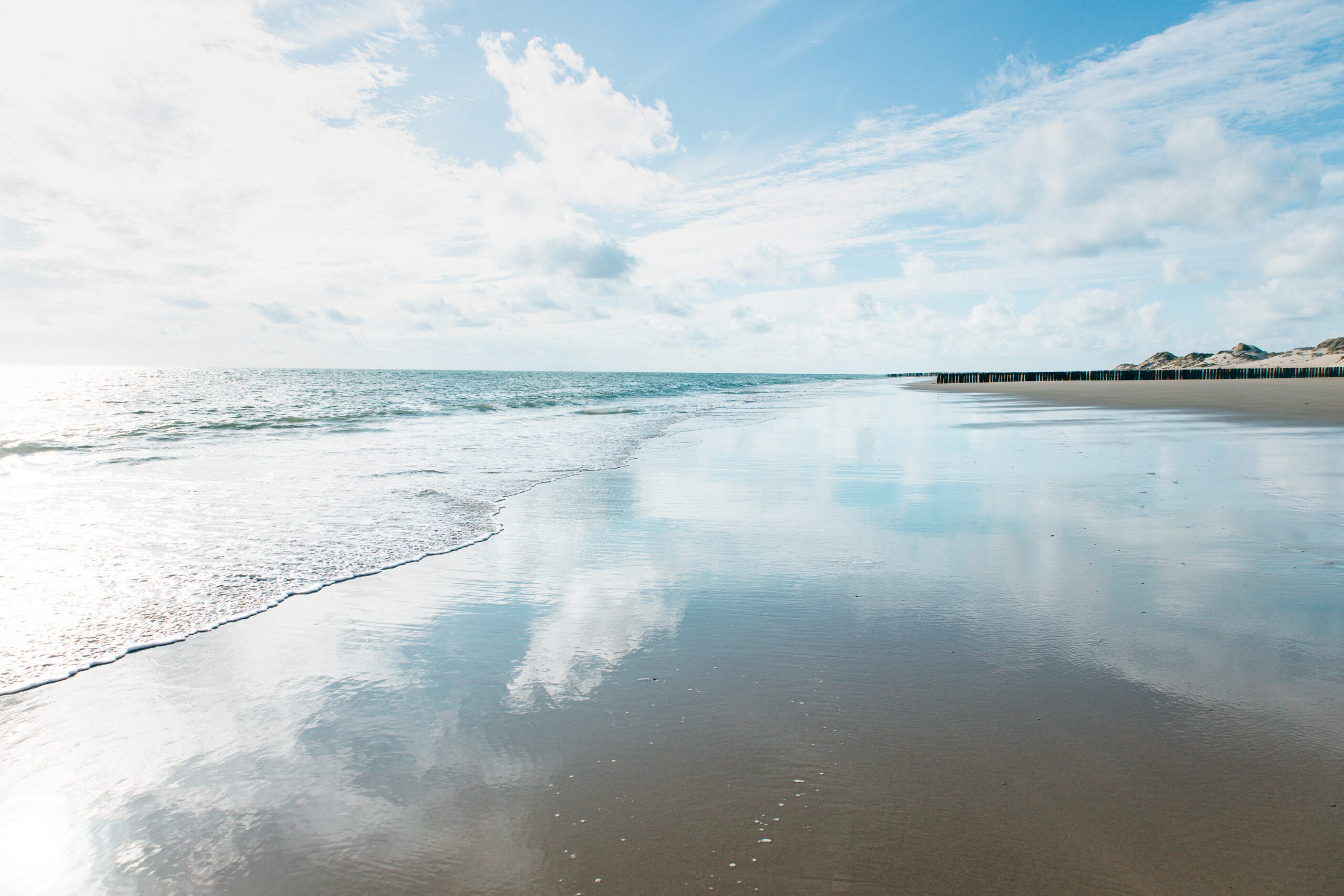Nasser Strand mit Spiegelung und Buhnen in Zeeland